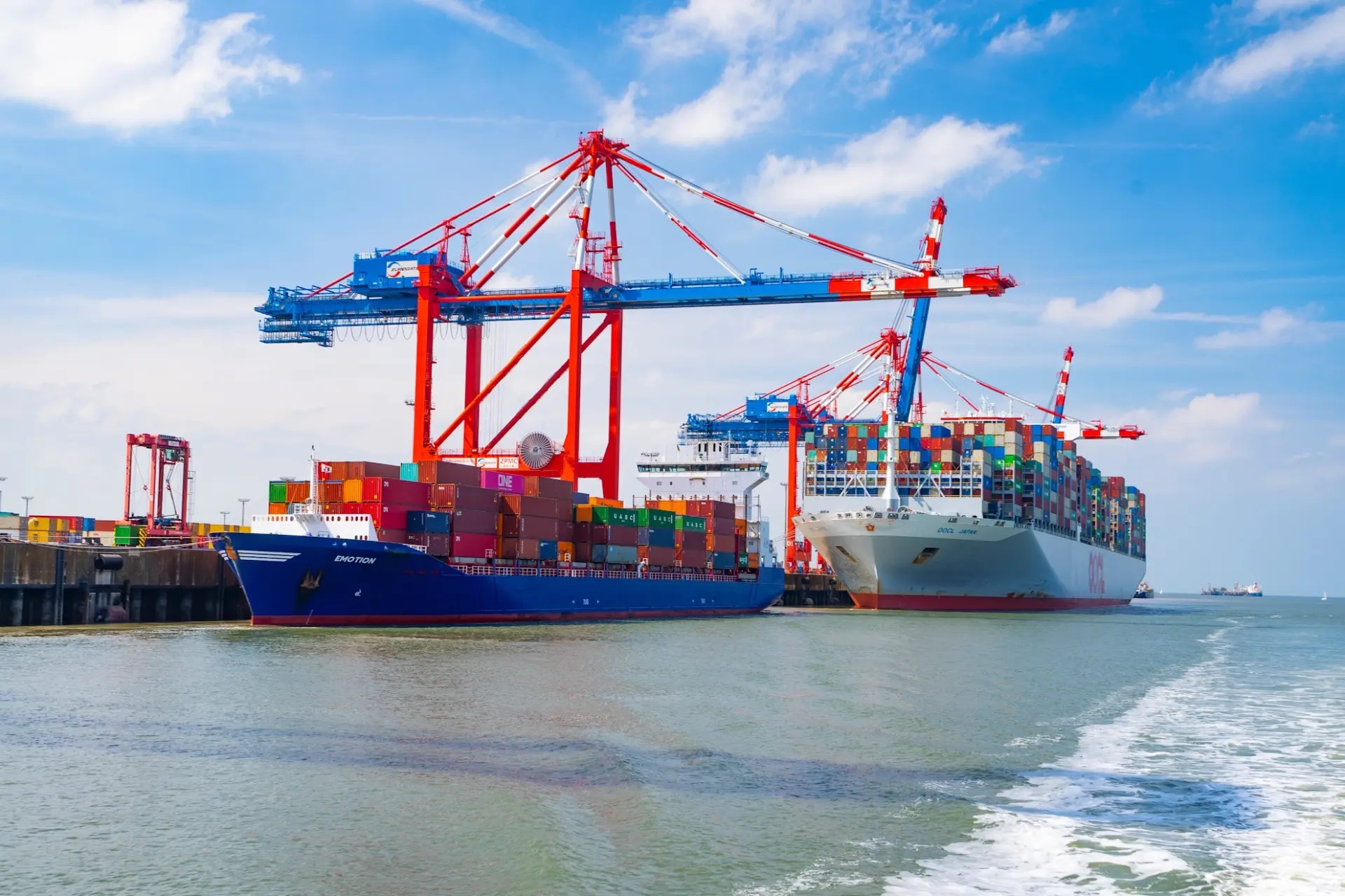 Deutschlands einziger Tiefwasserhafen: Jade Weser Port in Wilhelmshaven. Gr0ße Frachtschiffe mit Kränen und Kisten vor blauem Himmel.