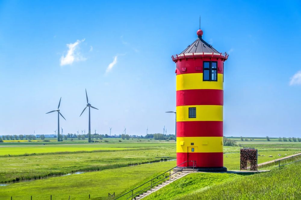 Niedersachsen setzt auf Windkraft: wie hier am gelb-rot gestreiften Leuchtturm in Greetsiel vor blauem Himmel.