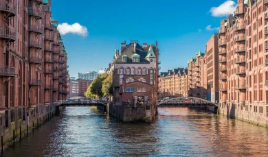 Ansicht eines historischen Backsteingebäudes zwischen zwei Kanälen, umgeben von Brücken und weiteren Gebäuden in einer Speicherstadt.